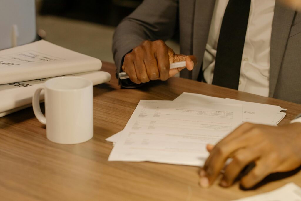 Free Close-up of a businessman holding and reviewing documents on a wooden desk. Stock Photo